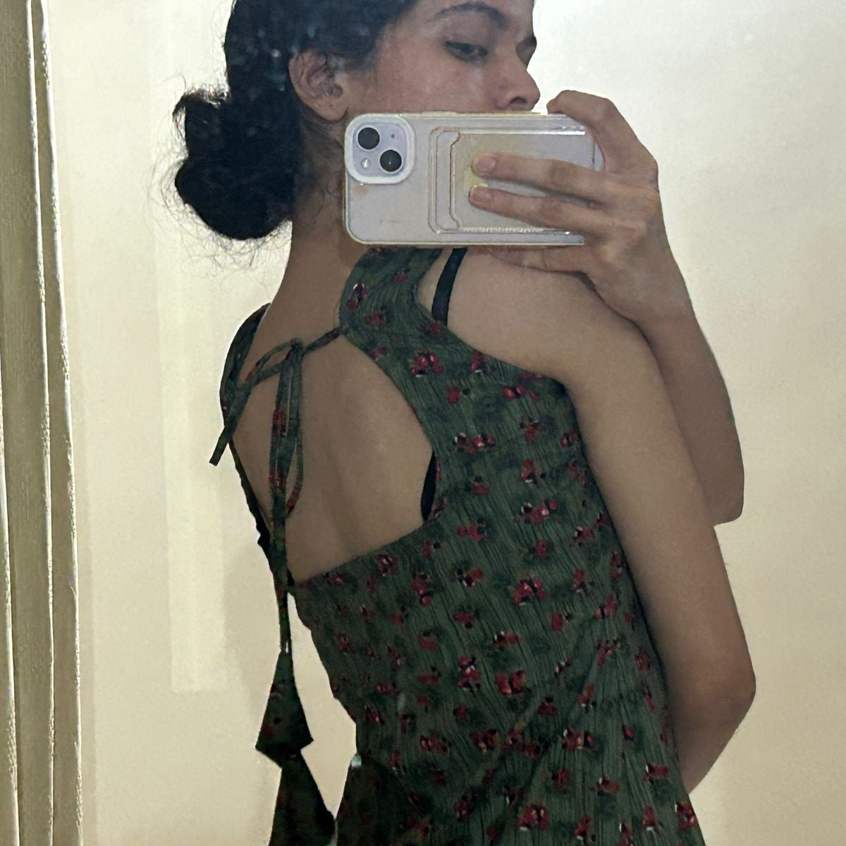 Person wearing a green dress with red patterns, taking a mirror selfie.